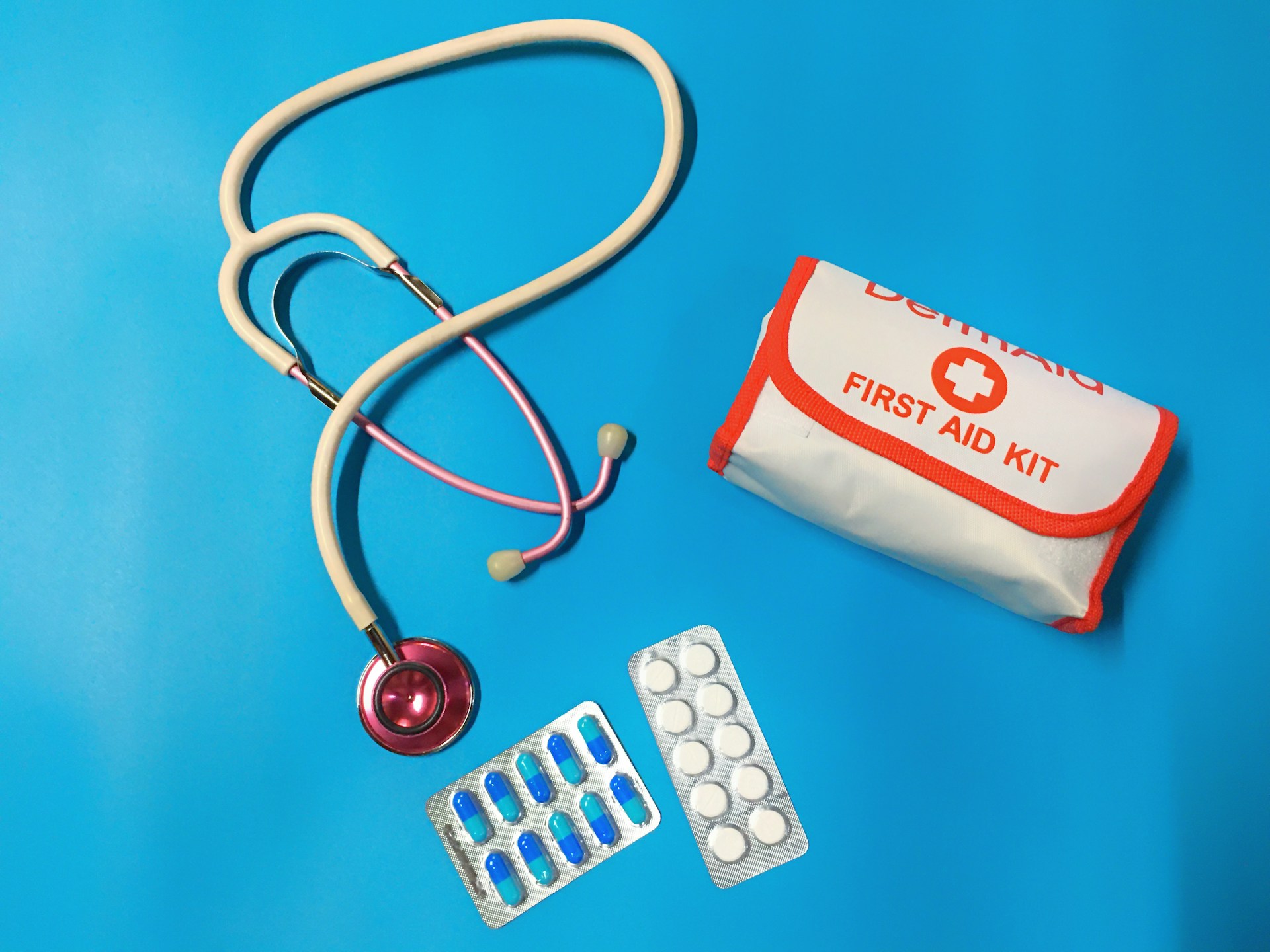 Stethoscope, first aid kit, and two blister packs of pills on a blue background